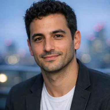 Dark-haired man in his early thirties, olive skin, casual blazer, relaxed expression